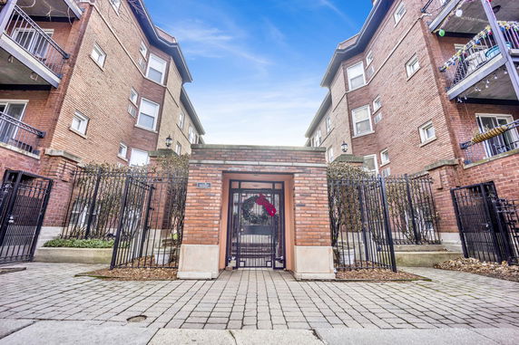 Front view of a brick apartment building with balconies and gated entrance.