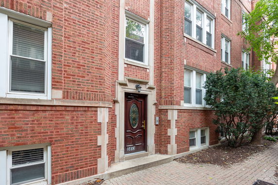 Front view of a brick apartment building with multiple windows and a wooden door.