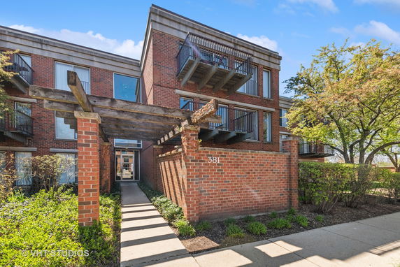 Front view of a multi-story brick building with balconies and a wooden pergola entrance.