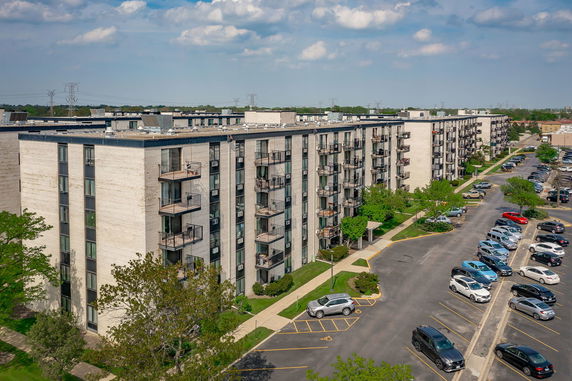View of multi-story apartment complex with balconies and adjacent parking area.