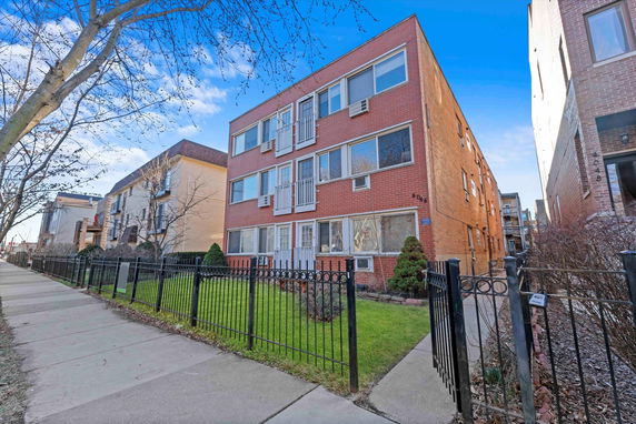 Front view of a three-story brick apartment building with a fenced yard.