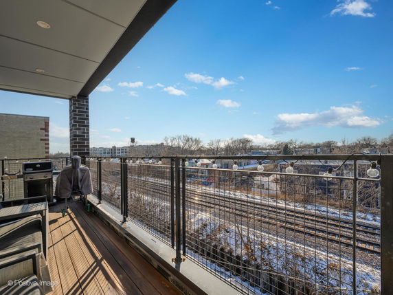 View from a building balcony showing a railroad and distant trees under a clear blue sky.