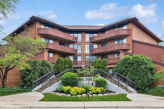 Front view of a multi-story building with multiple balconies and stairs leading up to the entrance.