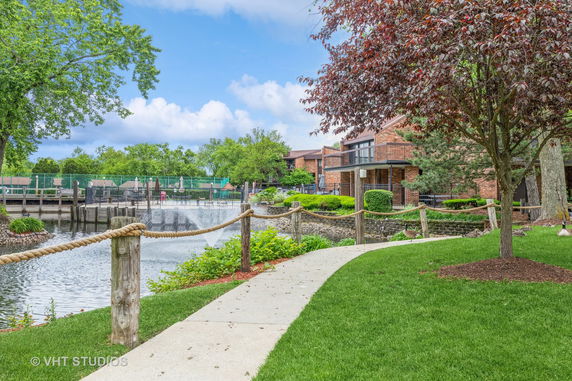 A path leading through a landscaped area with a view of a building adjacent to a pond and fountain.