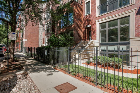 Front view of a red brick townhouse with gated entrance and large windows.