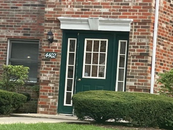 Front view of a brick house entrance with a green door and decorative white molding.