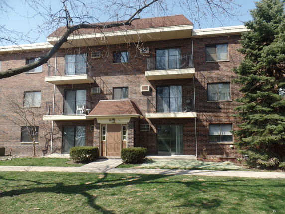 Front view of a three-story brick apartment building with balconies.