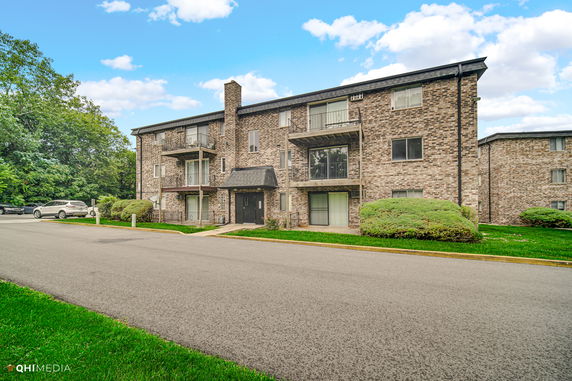 Front view of a three-story brick apartment building with balconies.