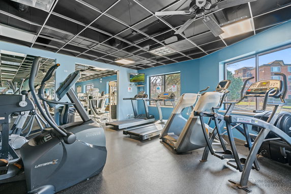 Interior view of a gym with various exercise equipment and large windows.