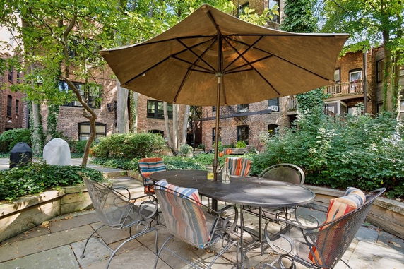 View of brick apartment building with patio furniture and umbrella in courtyard.