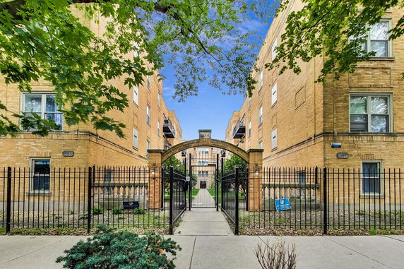 Front view of a brick apartment building with an arched entryway and gated entrance.
