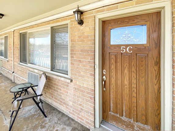 Front view of a building with a wooden door labeled 5C and a small outdoor seating area.