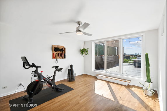 Room with exercise bike, ceiling fan, and storage for fitness equipment.