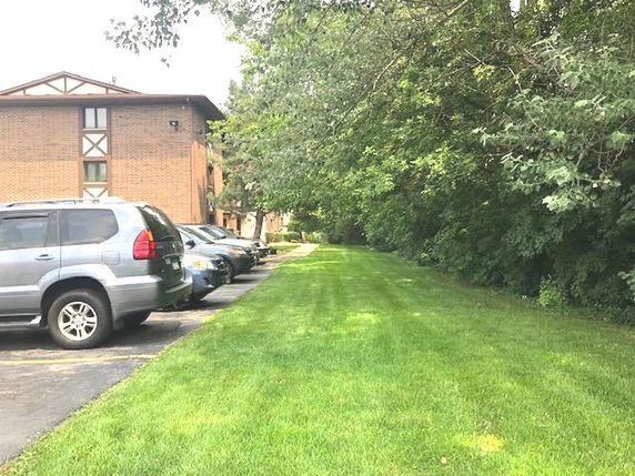 Outdoor parking area with several parked cars next to a brick apartment building.