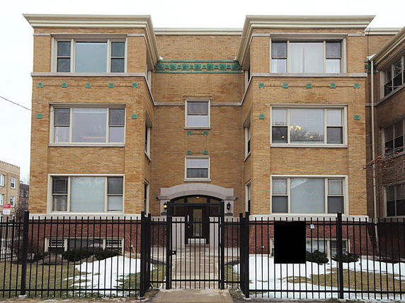Front view of a three-story brick apartment building with large windows and a gated entrance.
