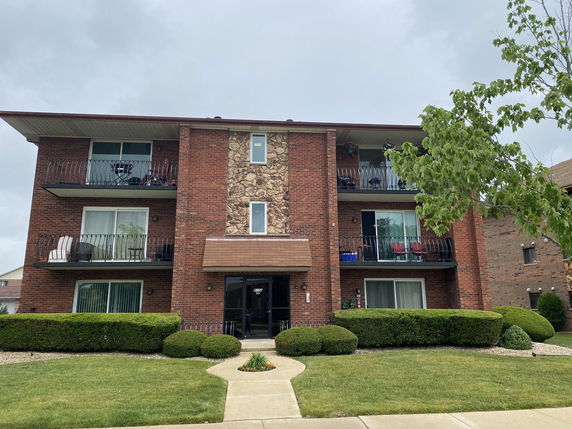 Front view of a three-story brick apartment building with balconies.
