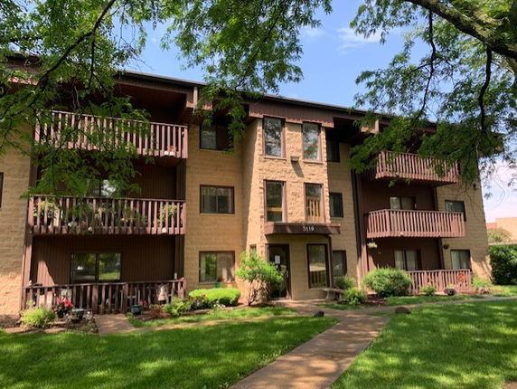 Front view of a three-story building with balconies and a landscaped entrance.