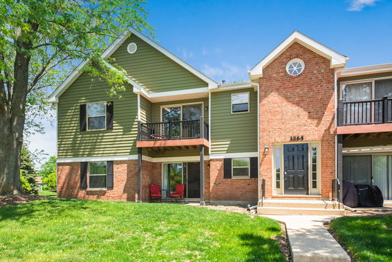 Front view of a two-story house with a mix of brick and green siding exterior, featuring a small balcony.