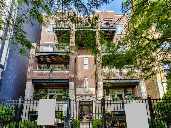 Front view of a multi-story brick building with balconies and a gated entrance.