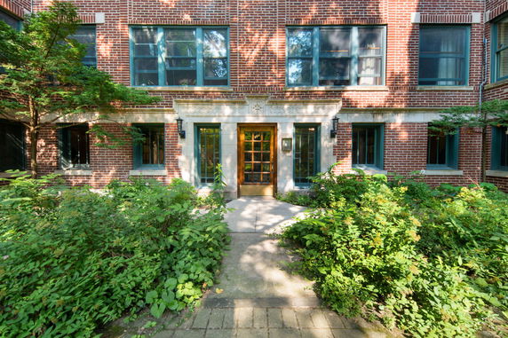 Front view of a brick apartment building entrance with large windows.