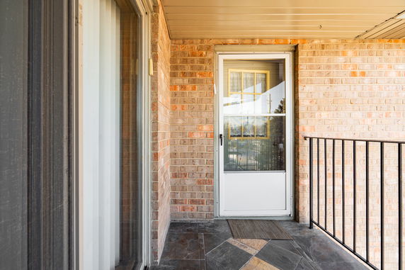 Front view of an entrance door with a tiled patio area and brick exterior.