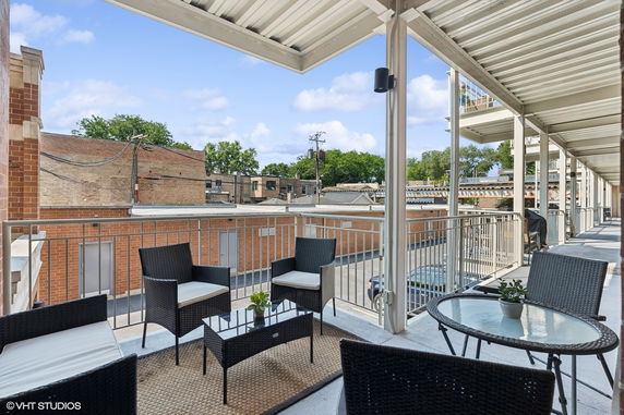 View from a covered outdoor balcony with furniture overlooking nearby buildings.