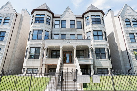 Front view of a multi-story stone building with prominent bay windows and a gated entrance.
