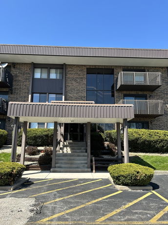Front view of a multi-story apartment building with balconies and an entrance staircase.