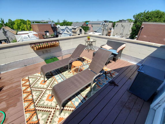 Rooftop terrace with lounge chairs, a small table, and decorative cushions on a patterned rug.
