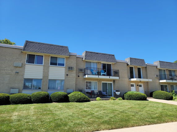 Front view of a multi-story residential building with balconies and lawn in front.