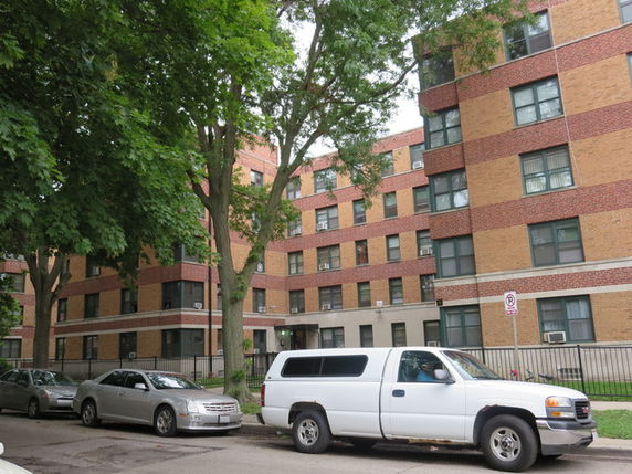 Front view of a multi-story brick apartment building with parked cars in front.