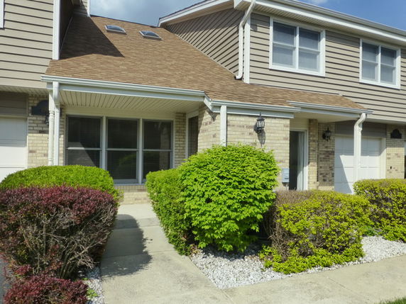 Front view of a two-story house with brown siding and shrubs in the front yard.