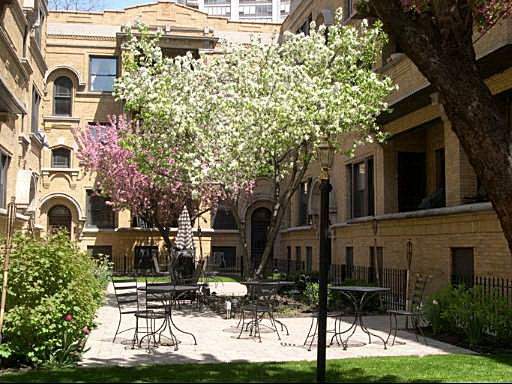 Courtyard view with outdoor seating, surrounded by brick buildings and blooming trees.