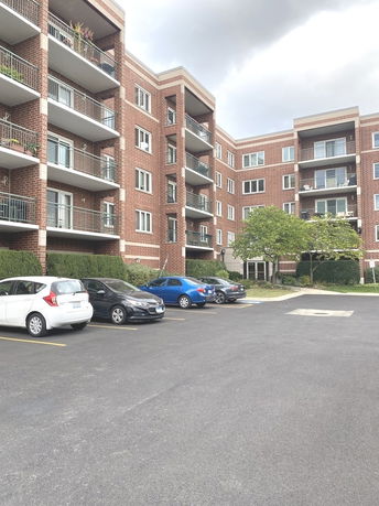 Parking area in front of a multi-story brick apartment building with balconies.