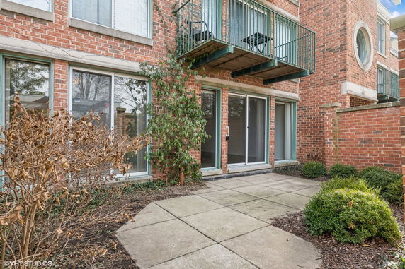 Front view of a brick residential building with small balconies and sliding glass doors at the ground level.
