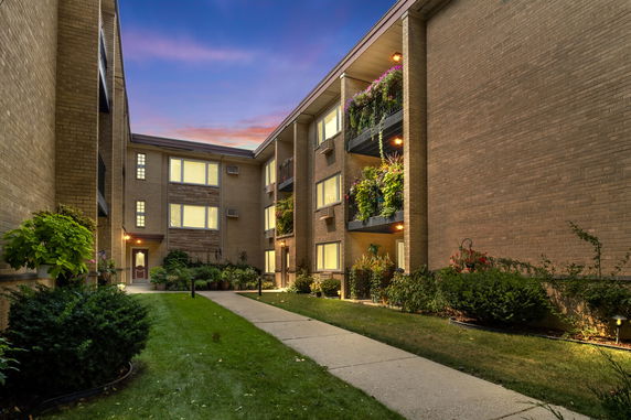Front view of a multi-story apartment building with balconies and illuminated windows.