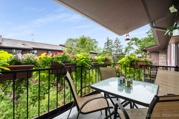 Balcony view with outdoor seating and plants overlooking rooftops and trees.