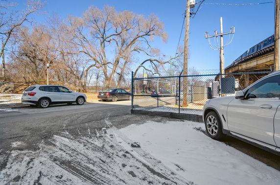 Outdoor parking area with several cars and a nearby train line.