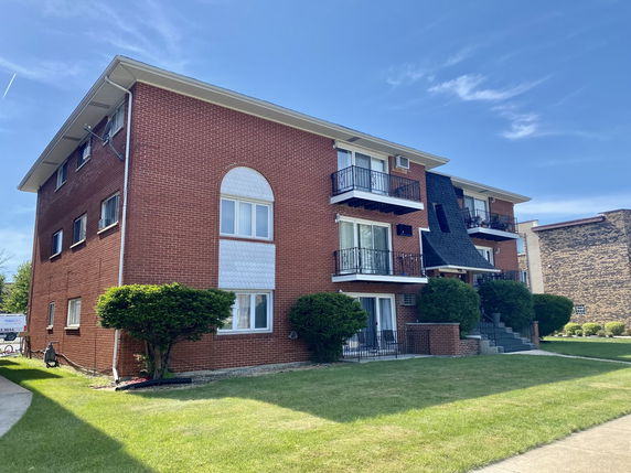 Front view of a three-story brick apartment building with balconies and stairs.