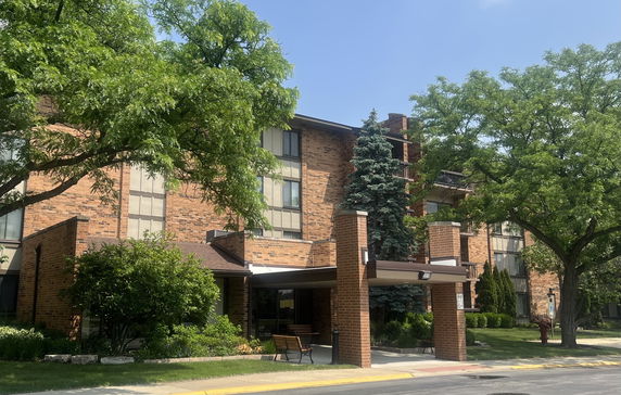 Front view of a multi-story brick building with large windows and surrounding greenery.