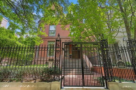 Front view of a multi-story brick house with iron gate and steps leading to the entrance.