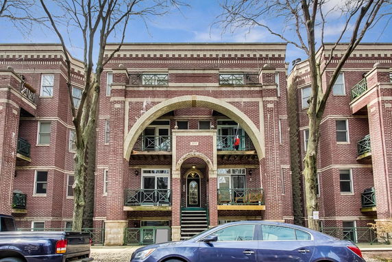 Front view of a brick apartment building with arched entryway and balconies.