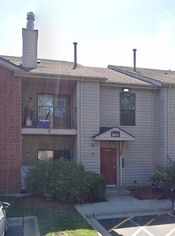 Front view of a two-story house with a balcony and and parking area.