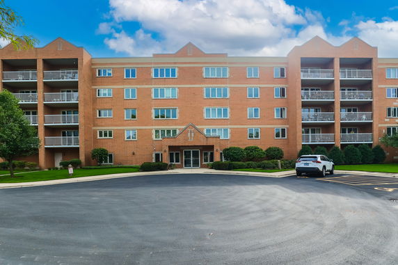 Front view of a four-story brick apartment building with balconies and a parking area.