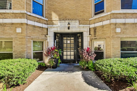 Front view of a brick building entrance with decorative plants.
