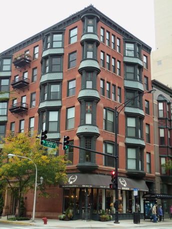 Front view of a multi-story brick building with bay windows and street-level shops.