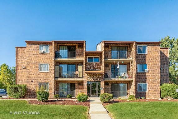 Front view of a three-story brick apartment building with balconies.