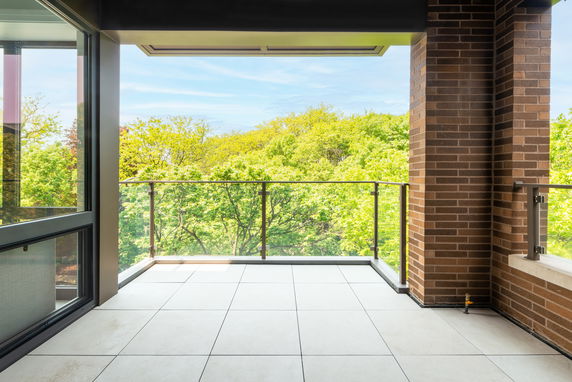 Balcony with glass railing overlooking a green treetop view.