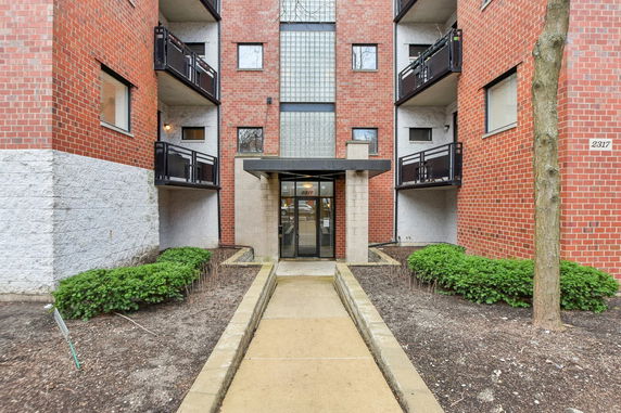 Front view of a multi-story brick apartment building with balconies and glass entrance.