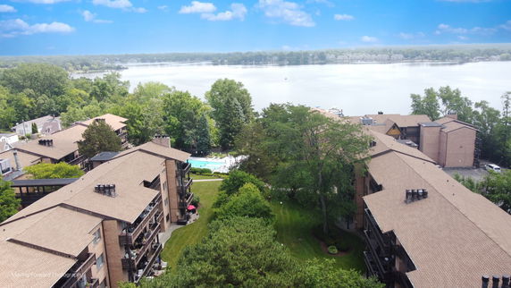 Panoramic view of a residential complex near a lake with a swimming pool and lush greenery.